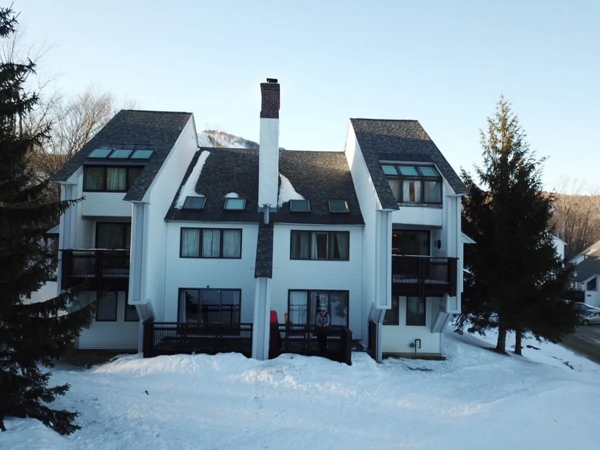 A cozy mountain lodging scene featuring balconies overlooking snow-covered ground. The inviting building is set against a wintry backdrop, conveying warmth and comfort amidst the snowy landscape.