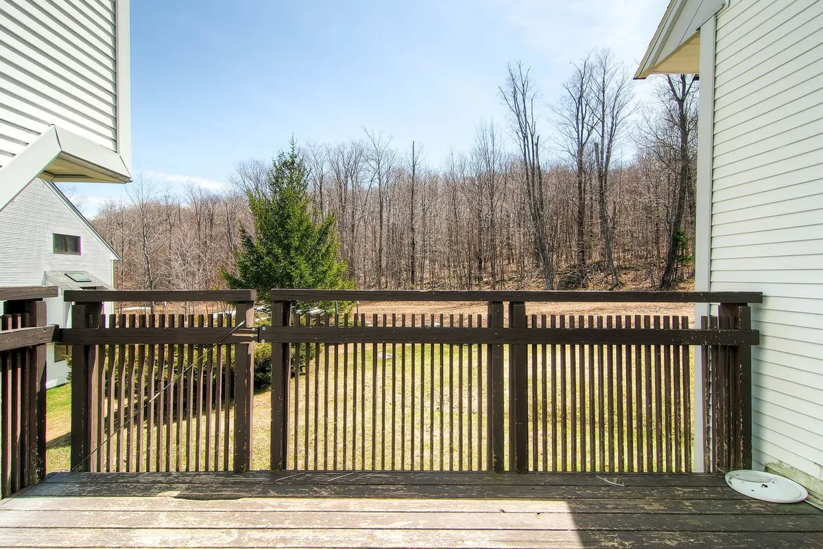 A view from the deck, featuring a wooden railing overlooking lush trees and open outdoor space. The peaceful scene suggests the transition from the interior living area to the outdoors, capturing the fresh mountain air and seasonal beauty described in the narrative.