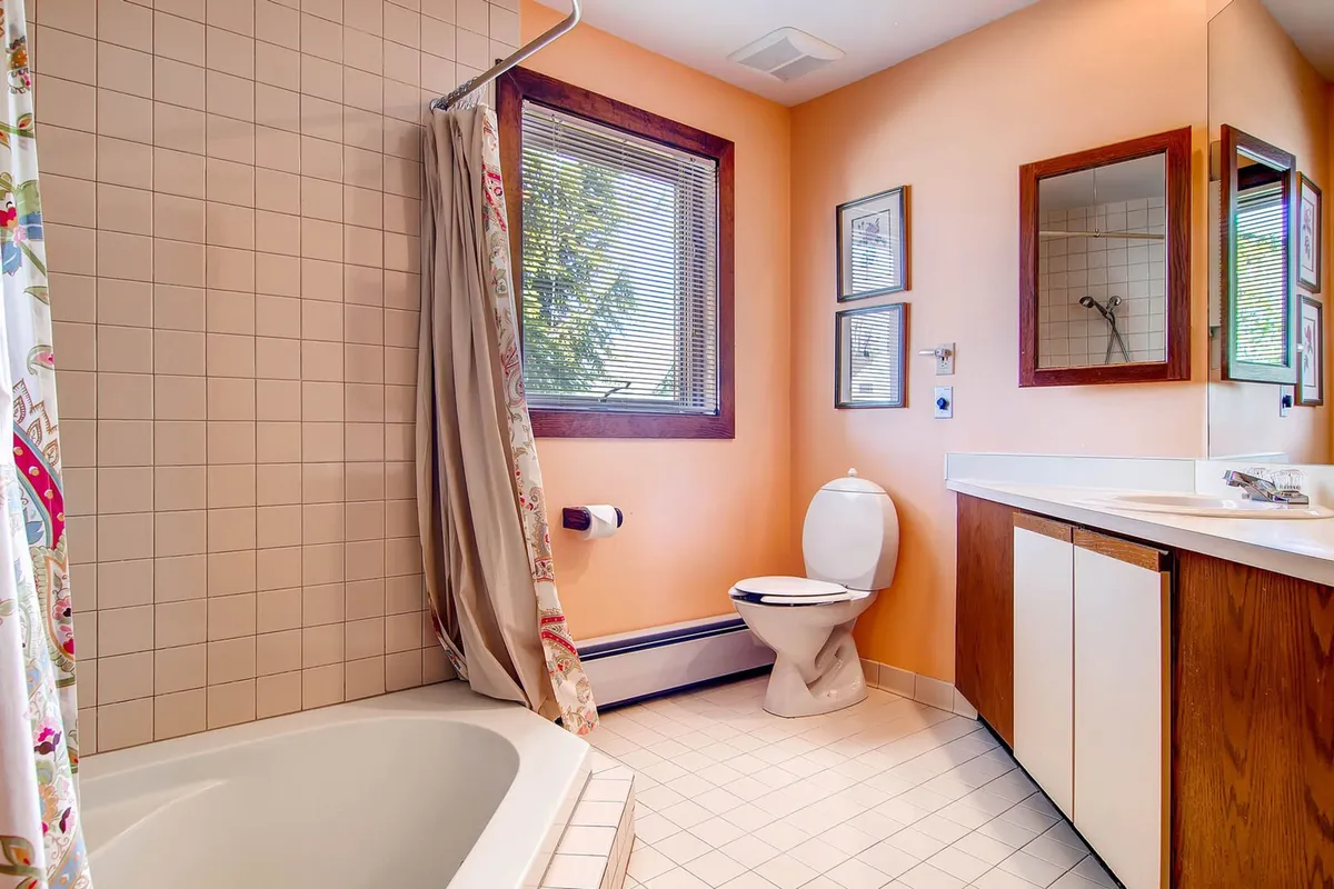 A bright, inviting bathroom featuring a large bathtub (suggestive of a whirlpool tub), sink, toilet, decorative shower curtain, and a window letting in plenty of natural light. The space feels serene and perfect for relaxation or soothing tired muscles after outdoor activities.