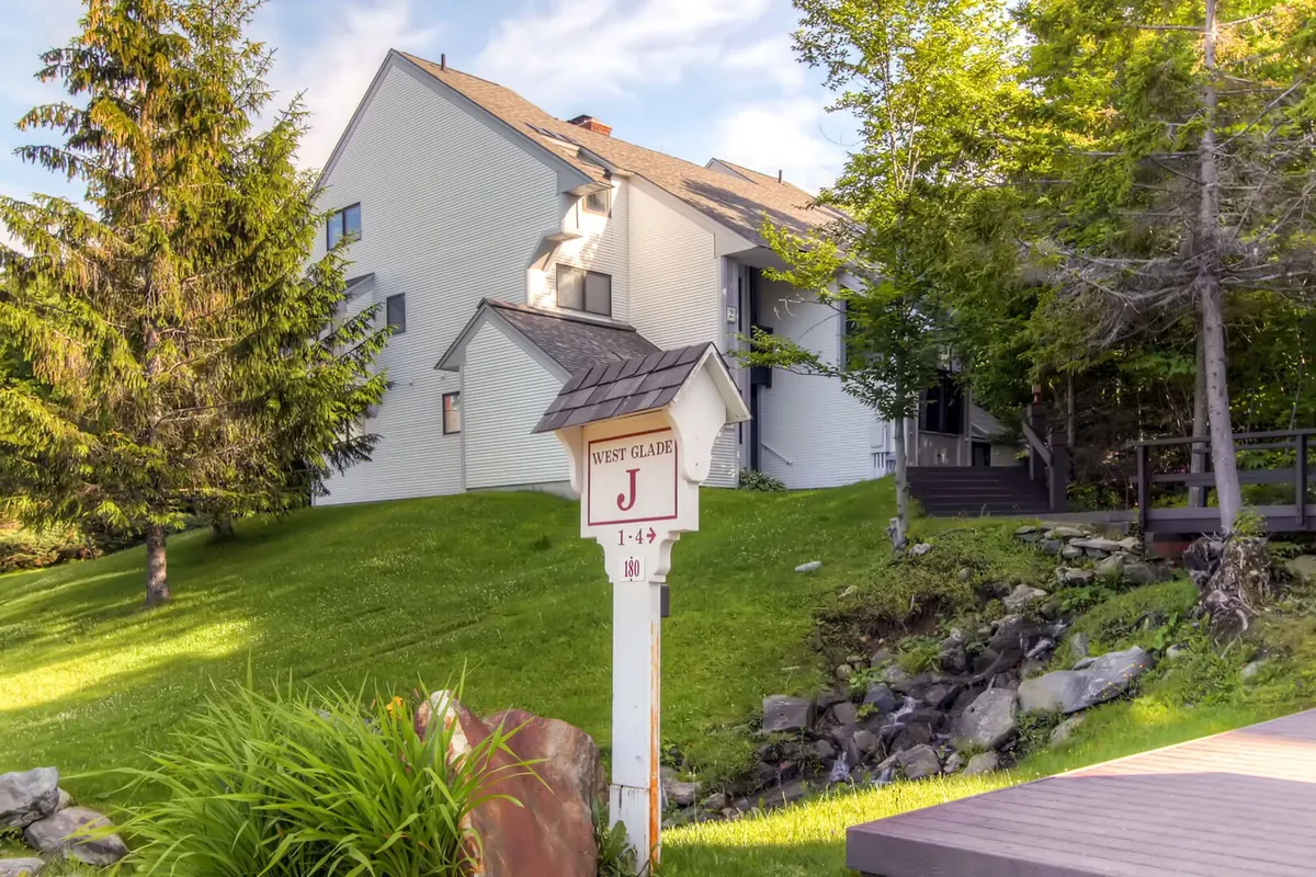 A welcoming exterior view of the building with a landscaped garden, signpost, and surrounding trees. The outdoor area appears accessible and inviting, hinting at nearby trails and natural exploration opportunities right outside your door.