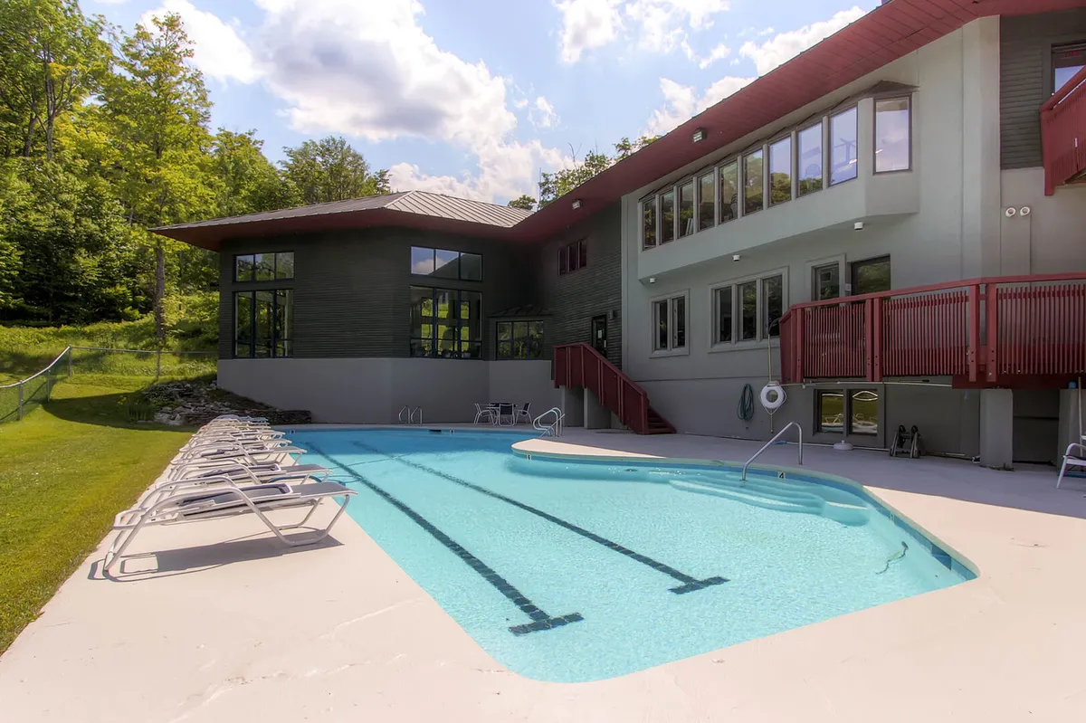 An inviting outdoor swimming pool set against modern resort architecture and lush greenery. The tranquil water sparkles under natural light, while comfortable lounge chairs line the sides, hinting at leisurely afternoons by the pool or early morning swims. The setting exudes relaxation and a resort-like atmosphere.